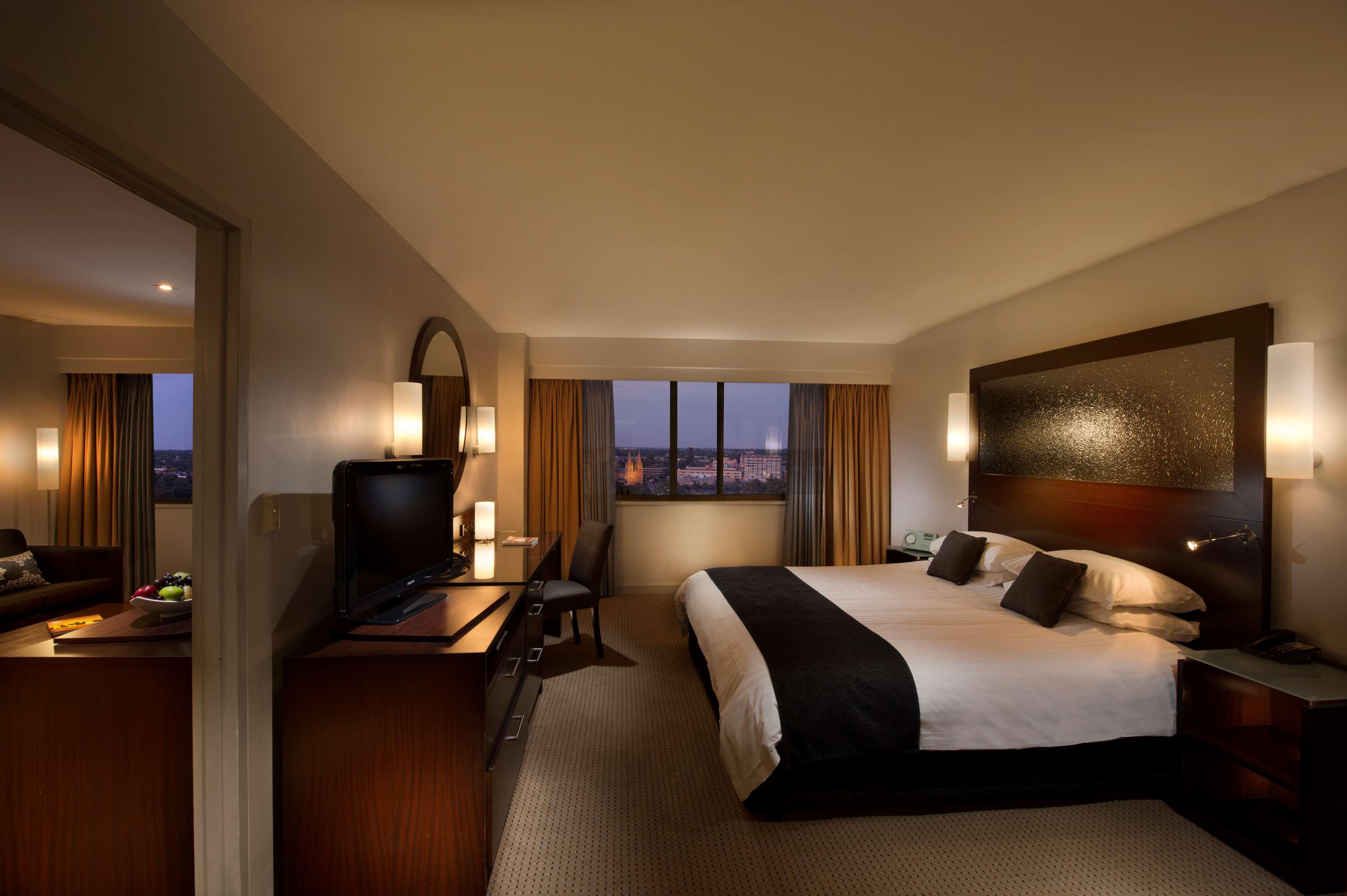 Stamford Plaza Adelaide Otel Dış mekan fotoğraf The photo features a modern hotel room that includes a large bed with dark and light bedding, complemented by two pillows. The room is well-lit with warm lighting and has a contemporary aesthetic. To one side, there is a wooden dresser with a flat-sc