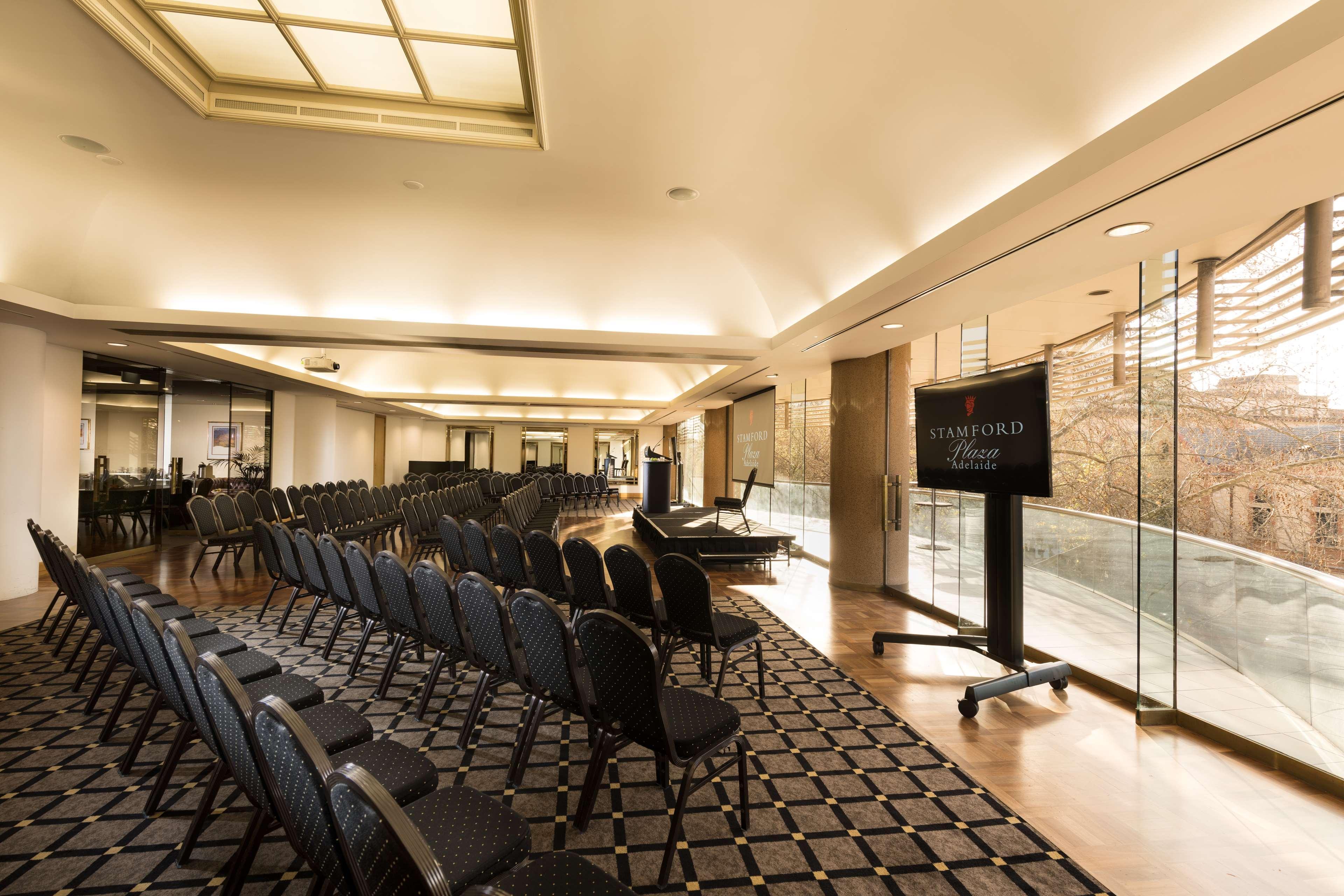 Stamford Plaza Adelaide Otel Dış mekan fotoğraf The photo shows a large, elegantly designed event space or meeting room. There are rows of black chairs set up facing a presentation area. The flooring features a patterned carpet, and large windows allow natural light to enter the room. On one side,