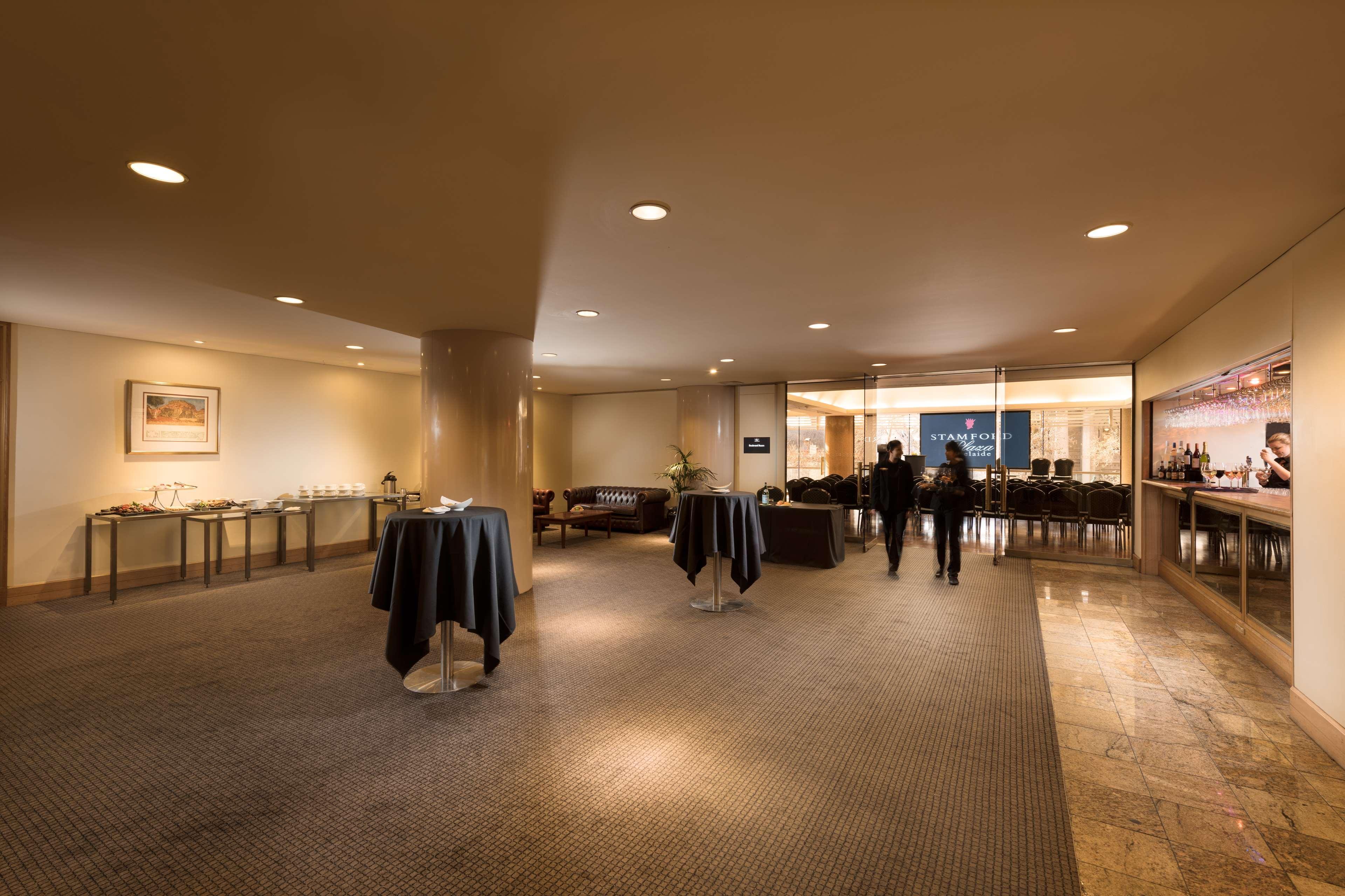 Stamford Plaza Adelaide Otel Dış mekan fotoğraf The image shows an indoor space that appears to be a lounge or reception area. There are several round tables with dark tablecloths positioned throughout the room. The floor is carpeted, and the lighting is warm and somewhat dim. In the background, t