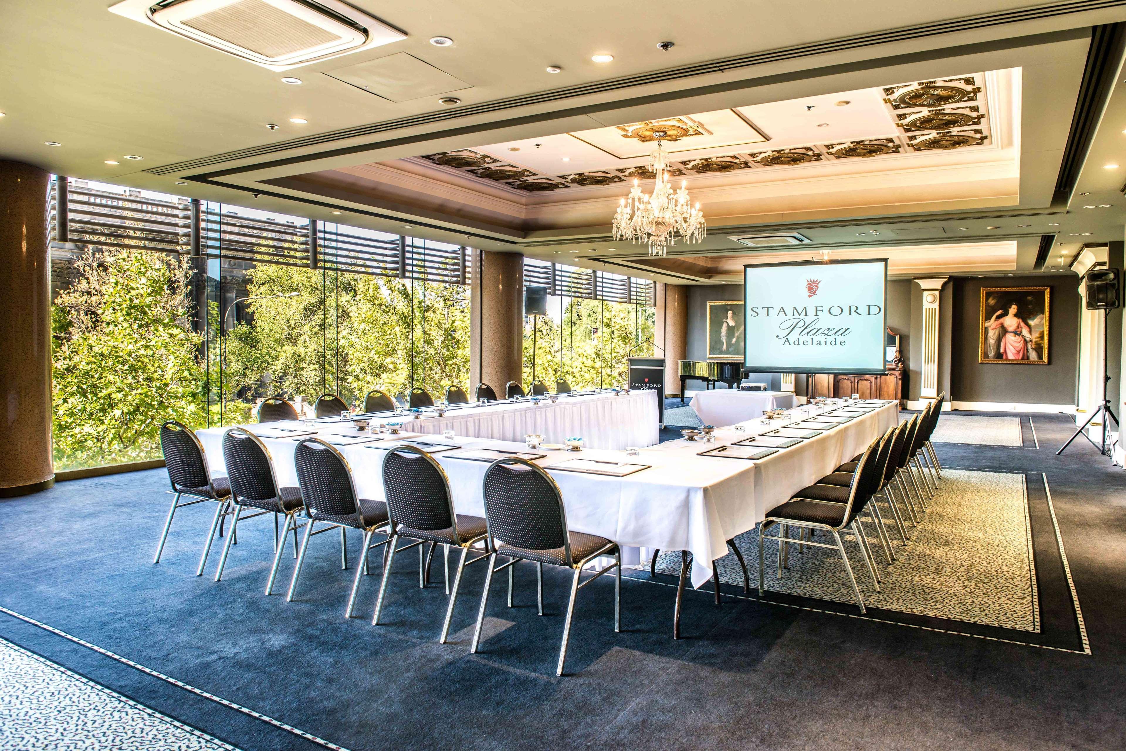 Stamford Plaza Adelaide Otel Dış mekan fotoğraf The photo shows a stylish conference room set up for a meeting or event. There is a long rectangular table covered with a white tablecloth, surrounded by black chairs. A large screen displays the name "Stamford" along with a logo. The room features l